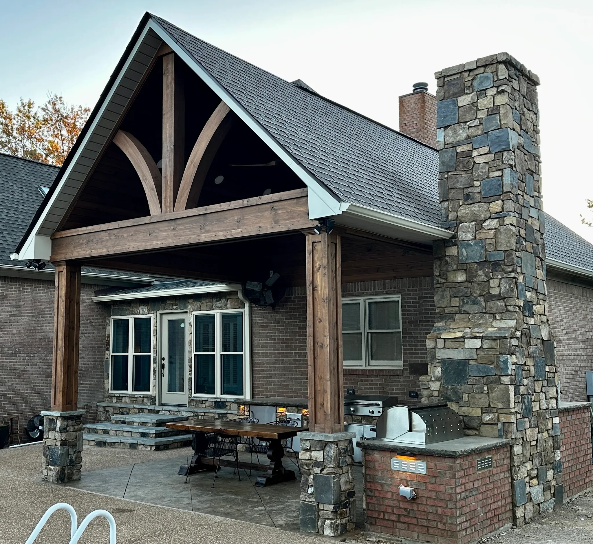 A timber-gable covered patio with a stone chimney and outdoor kitchen